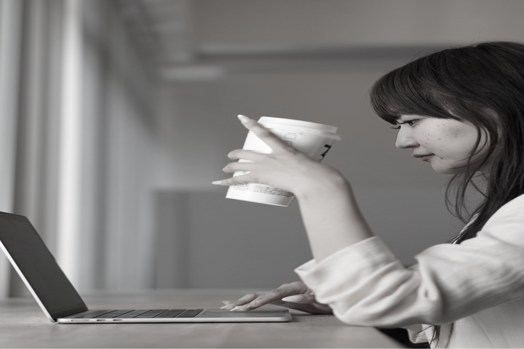 コーヒーを片手にノートパソコンへ向かう社員